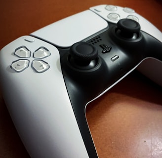 A gaming controller is placed on a wooden surface, featuring a sleek black and white design with prominent joysticks and buttons.