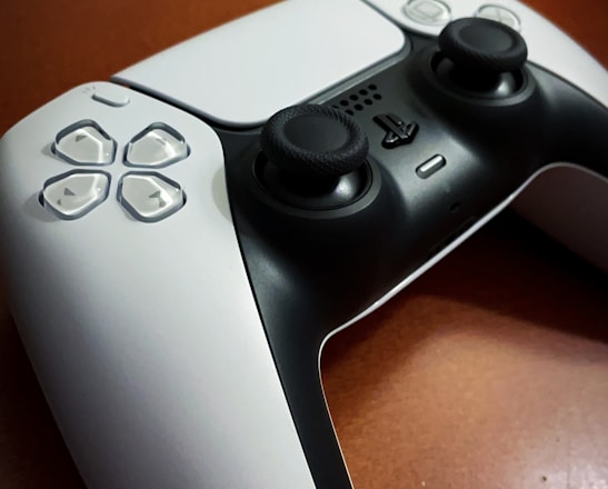 A gaming controller is placed on a wooden surface, featuring a sleek black and white design with prominent joysticks and buttons.