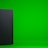 A black, rectangular gaming console stands upright against a vibrant green background. The console has a simple, sleek design with minimalistic features including a disc slot and a few buttons.