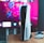 A gaming console is placed on a wooden table with a game controller nearby. In the background, a television screen displays colorful graphics, including geometric shapes and vibrant colors.