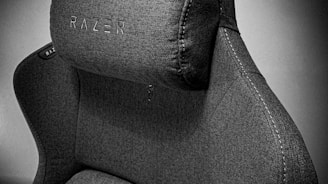 A high-quality, fabric gaming chair featuring ergonomic design and enhanced comfort. The chair has a distinct headrest with visible stitching, embossed branding, and a modern aesthetic.